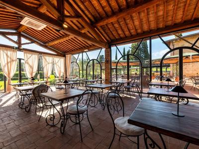 Krytá venkovní část restaurace s kovanými stoly a židlemi pod dřevěnou střechou.