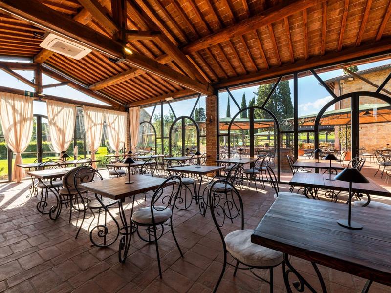 Krytá venkovní část restaurace s kovanými stoly a židlemi pod dřevěnou střechou.