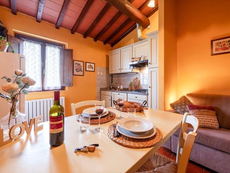Útulná jídelna s dřevěným stolem, židlemi, vínem, občerstvením a otevřenou kuchyní pod viditelnými dřevěnými trámy.