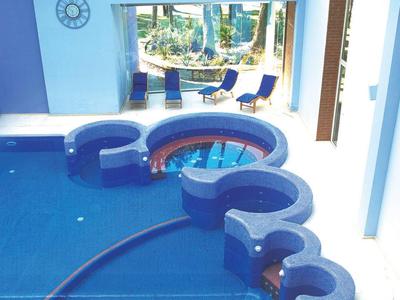 Modderne binnenzwembad met geïntegreerd bubbelbad en blauwe ligstoelen bij het raam