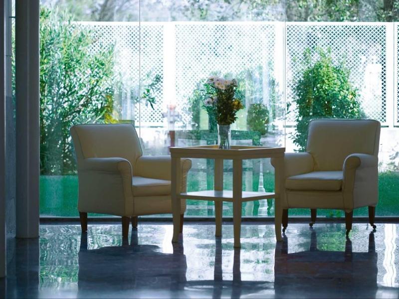 Two comfortable armchairs and a table with flowers in front of large windows and green outdoor area