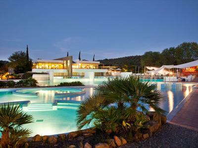 Hotel mit beleuchtetem Pool und Palmen bei Dämmerung, entspannte Urlaubsatmosphäre.