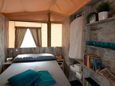 Gemütliches Hotelzimmer mit Doppelbett, Holzverkleidung und offenem Fenster mit Vorhängen.