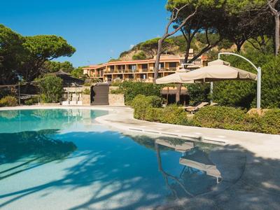 Großer Pool mit klar blauem Wasser, umgeben von grünen Bäumen und einem mehrstöckigen Gebäude.