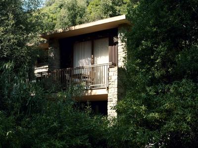 Una casa con balcón rodeada de densa vegetación verde y árboles.
