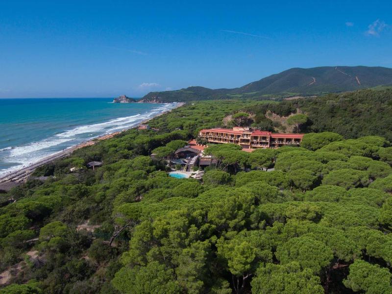 Hotel in un paesaggio costiero verdeggiante con vista sulla spiaggia e sul mare blu sotto un cielo sereno