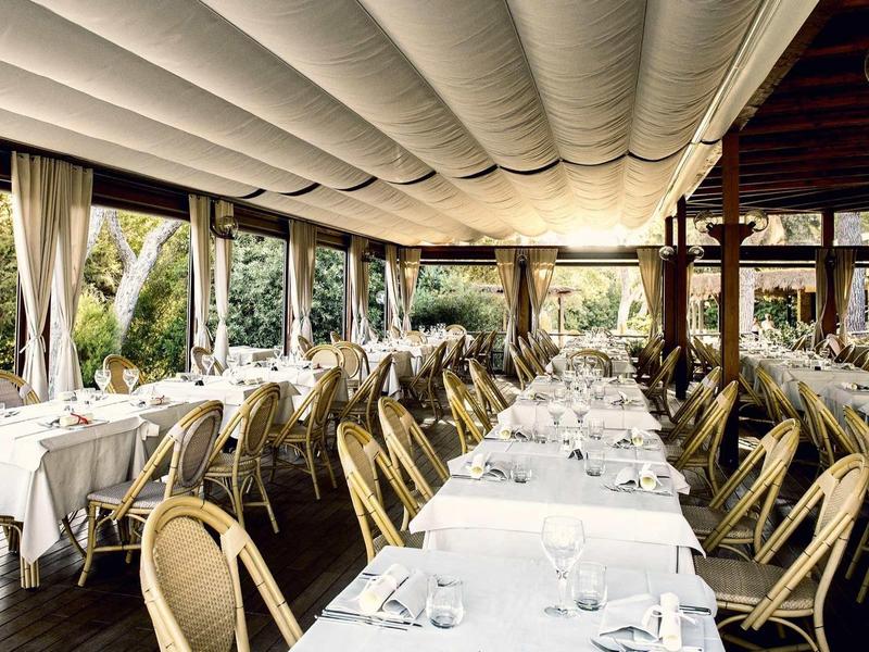 Ristorante elegante con tovaglie bianche e sedie in legno sotto un'area coperta.