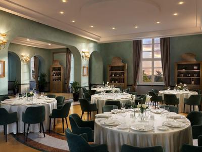 Elegancka sala restauracyjna hotelu z nakrytymi stołami, zielonymi ścianami i dużymi oknami.