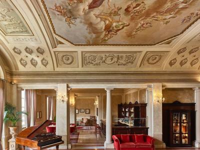 Elegancka lobby hotelowa z klasycznym malowidłem sufitowym, czerwonymi aksamitnymi sofami i fortepianem.