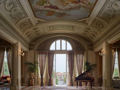 Elegancki korytarz hotelowy z dywanem, żyrandolami, dużymi oknami i fortepianem przy oknie.