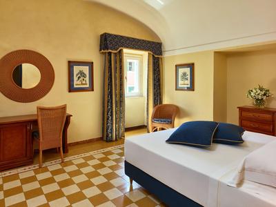 Jasny pokój hotelowy z podwójnym łóżkiem, biurkiem, krzesłem i dekoracyjnymi obrazami na ścianach.