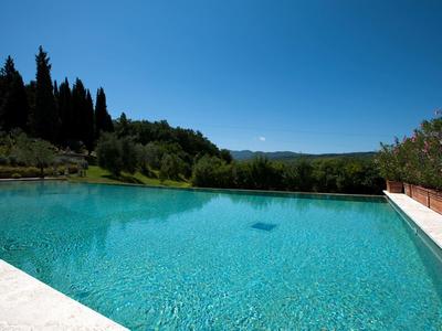 Outdoor pool with clear water surrounded by green trees and blue sky.
