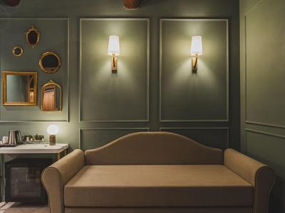 Elegantes Hotelzimmer mit braunem Sofa, dunklen Wänden und zwei Wandlampen.