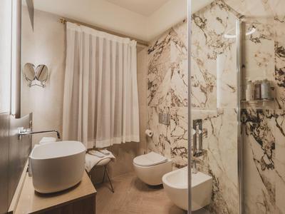 Modernes Badezimmer mit Marmorwänden, Dusche, Waschbecken und Toilette in hellem Ambiente.