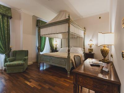 Elegantes Hotelzimmer mit Himmelbett, grünem Sessel und Holzboden.