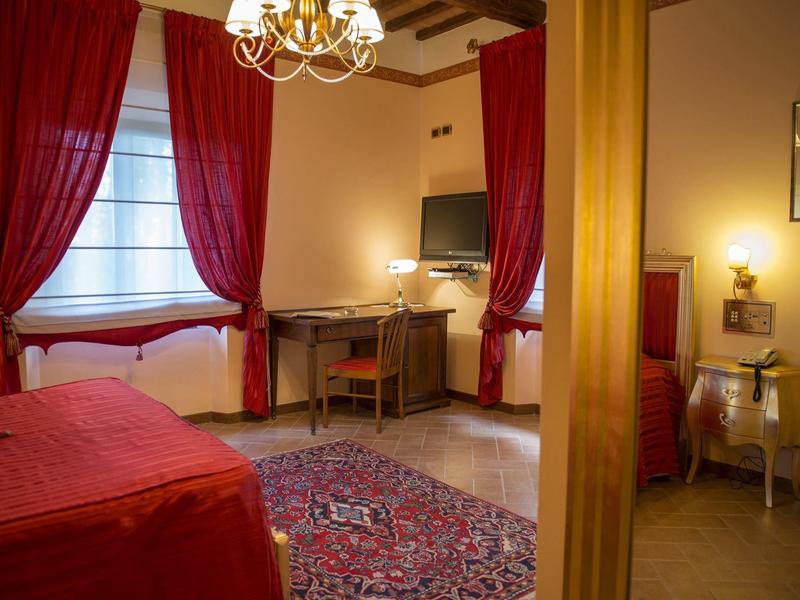 Cozy hotel room with red carpet, curtains, and desk with chair.