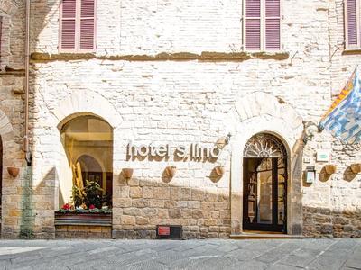 Jasno oświetlona kamienna elewacja hotelu z wejściami i flagami.