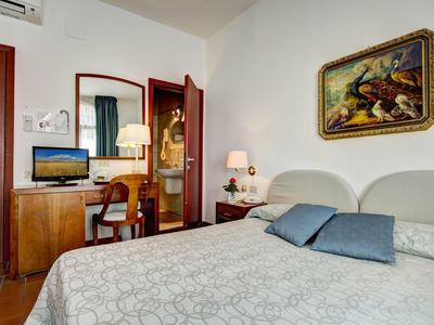 Przytulny pokój hotelowy z podwójnym łóżkiem, biurkiem, krzesłem, telewizorem i dekoracyjnym obrazem.