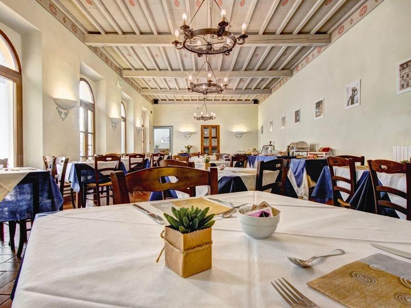 Jasna sala restauracyjna hotelu z drewnianymi meblami i dekoracyjnymi roślinami na białych obrusach.