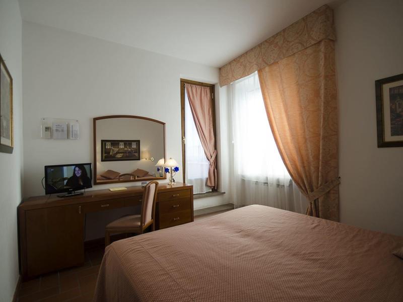 Przytulny pokój hotelowy z łóżkiem, biurkiem, krzesłem i oknem z zasłonami.