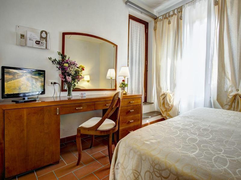 Jasny pokój hotelowy z drewnianym biurkiem, krzesłem, telewizorem i oknem z zasłonami.