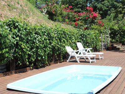 Small pool with white lounge chairs and green vegetation on a wooden terrace.