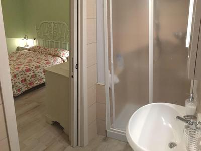Bathroom with shower cabin and sink, next to a bedroom with floral bedspread visible.