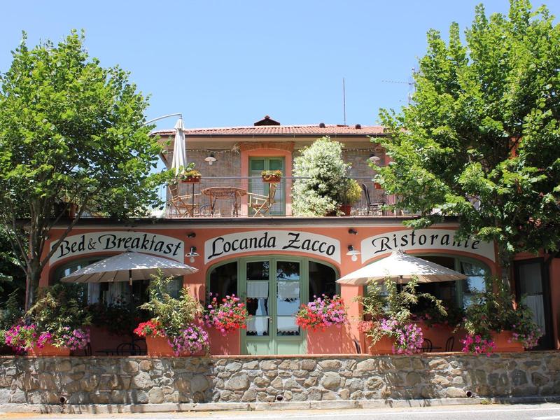 Facade of a restaurant with terrace, green trees, and colorful flowers.