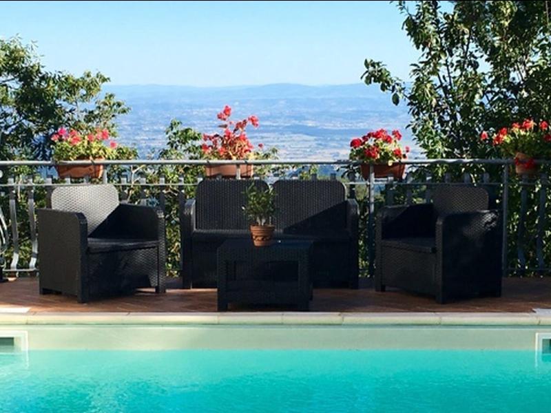 Three black lounge chairs by a pool overlooking mountains and flowers.