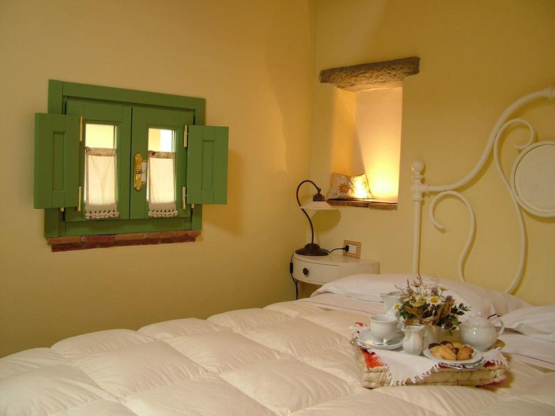 Cozy bedroom with green window shutters and white bed under warm lighting.