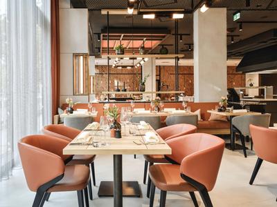 Modernes Restaurant mit hölzernen Tischen, bequemen rosa Stühlen und schicker Beleuchtung.