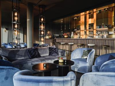 Elegante Hotelbar mit samtblauen Sesseln, runden Tischen und warm beleuchtetem Barbereich.