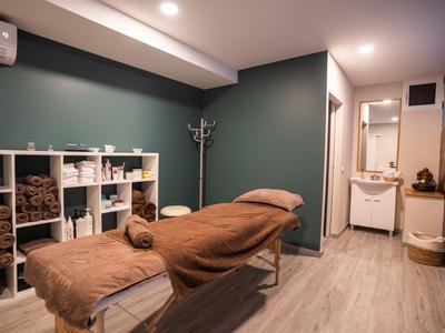 Gemütlicher Massageraum mit beiger Liege, grünem Wandton und Holzregal.