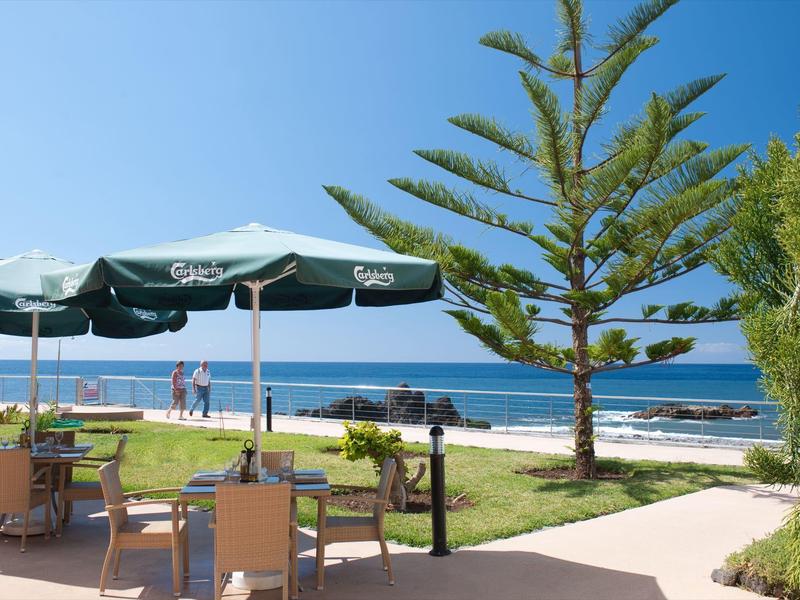 Espace extérieur avec parasols près d'un chemin herbeux et vue sur l'océan sous un ciel clair.