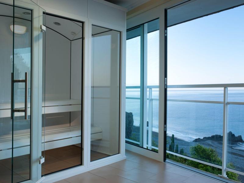 Chambre moderne avec portes vitrées et balcon donnant sur la mer et la côte.