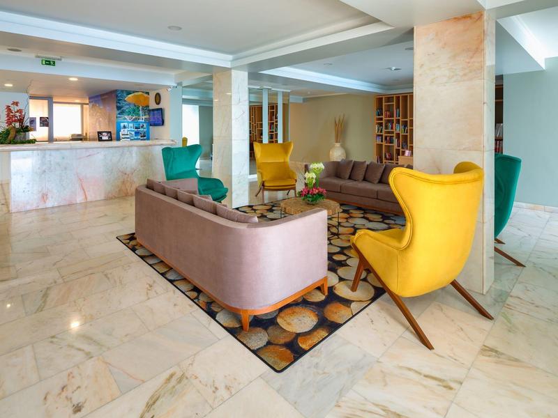 Hall d’hôtel moderne avec sol en marbre, fauteuils colorés, canapé et comptoir d’accueil.