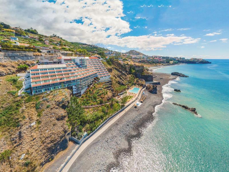Hôtel côtier construit sur des falaises surplombant une mer turquoise claire et une plage rocheuse.