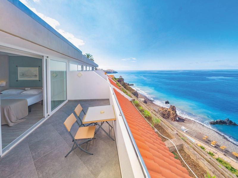 Balcon avec chaises donnant sur la mer et la route côtière depuis une chambre d'hôtel.