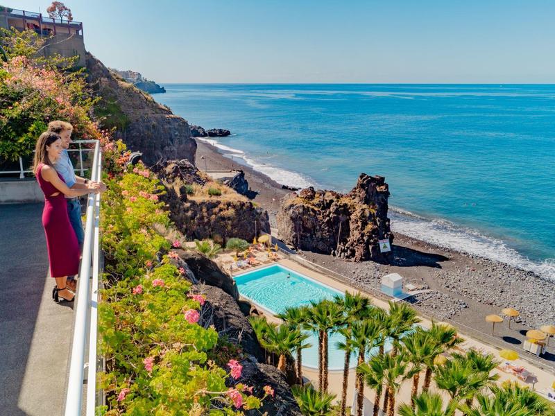 Femme admirant la vue sur l'océan depuis un balcon au bord d'une falaise près de la piscine et de la plage.