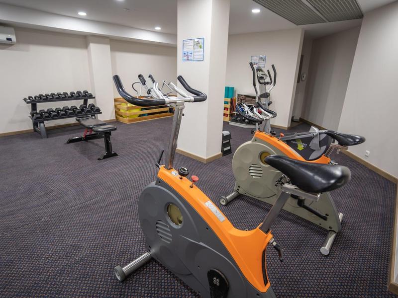 Salle de sport avec vélos d'exercice, poids et divers équipements de fitness sur moquette.