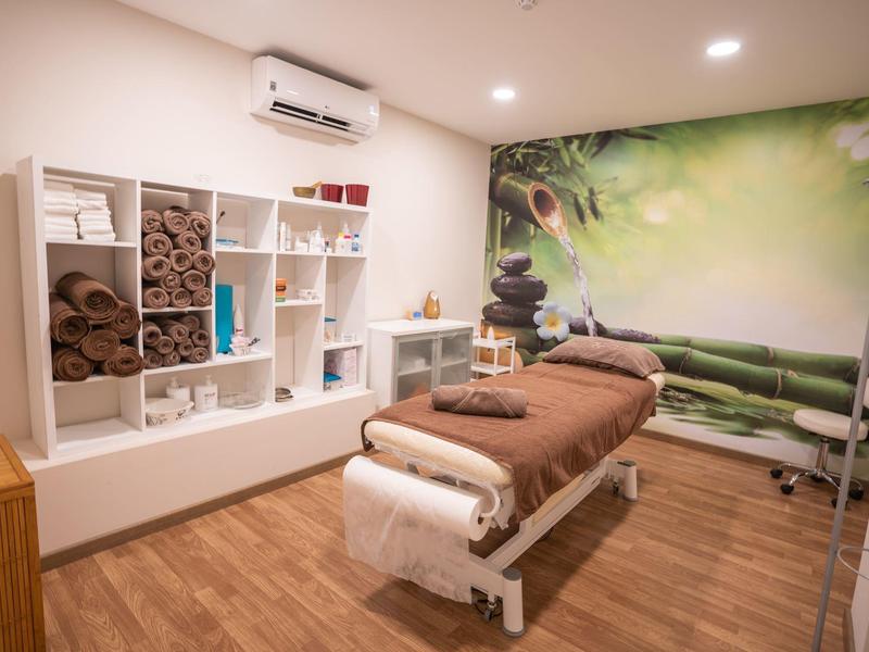 Salle de spa relaxante avec table de massage, étagères à serviettes et fresque murale nature.