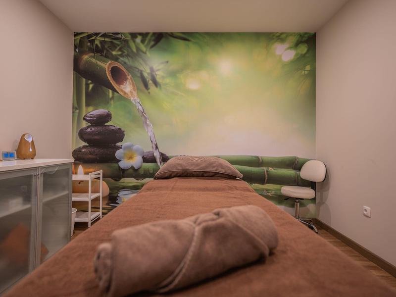 Salle de spa confortable avec table de massage, serviette et fresque murale nature verte apaisante.