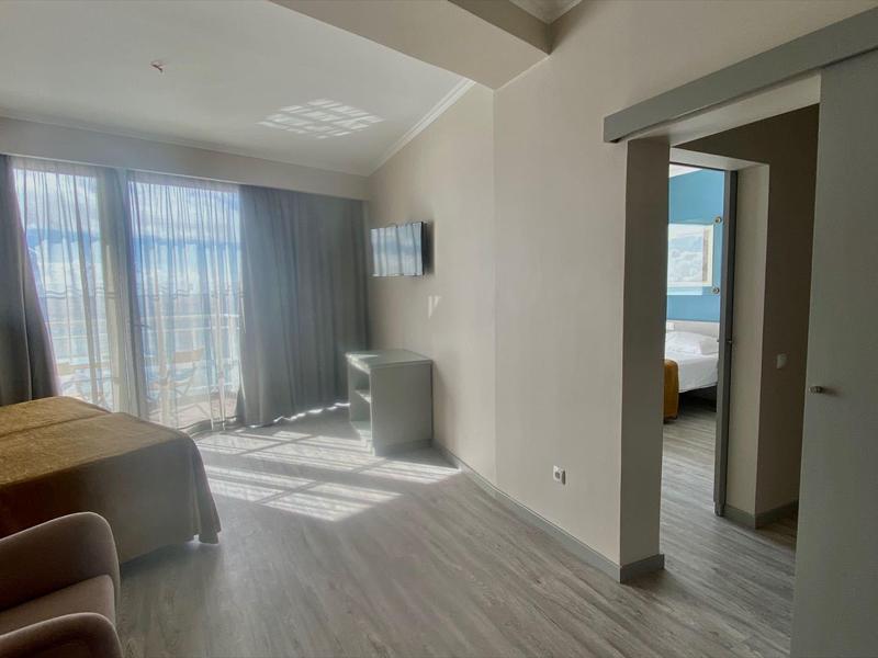 Chambre d'hôtel moderne avec lit, fauteuil, bureau et grande fenêtre avec rideaux transparents.