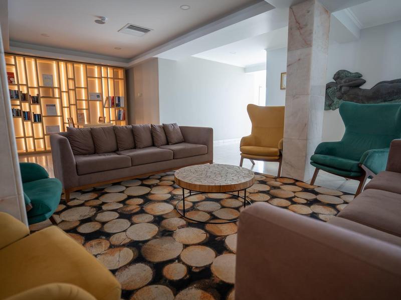 Coin salon confortable avec canapés, fauteuils colorés et tapis à motifs dans un hall d'hôtel.