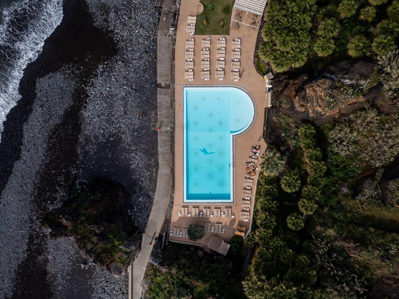 Vue aérienne d'une piscine près d'une plage avec des chaises longues et de la verdure.