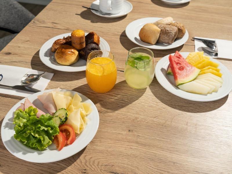Table avec petit-déjeuner comprenant jus, fruits frais, salade et viennoiseries sur surface en bois.