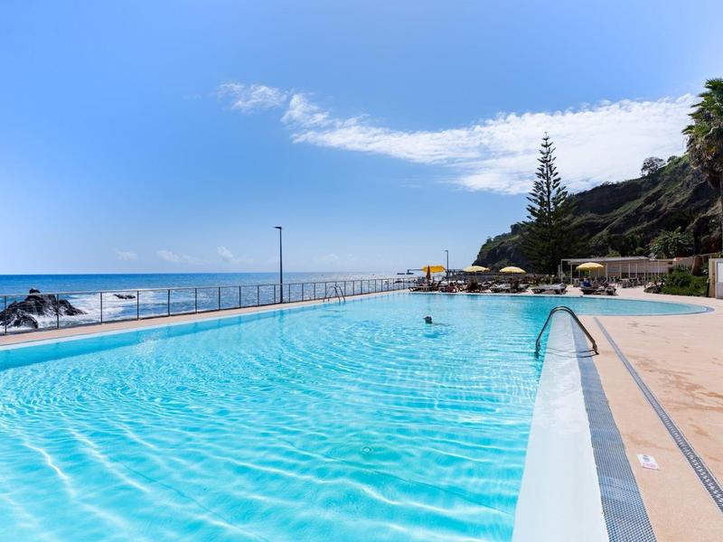 Piscine extérieure à l'eau claire près de l'océan et sous un ciel ensoleillé.