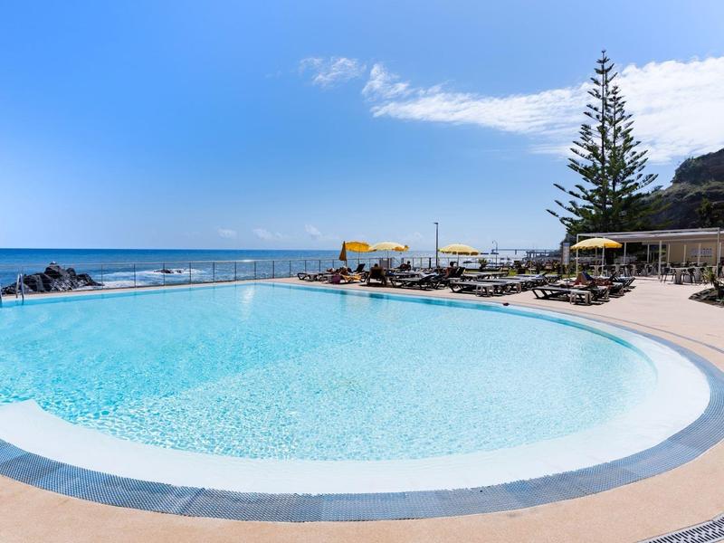 Piscine extérieure courbée avec eau claire donnant sur l'océan et chaises longues par une journée ensoleillée.
