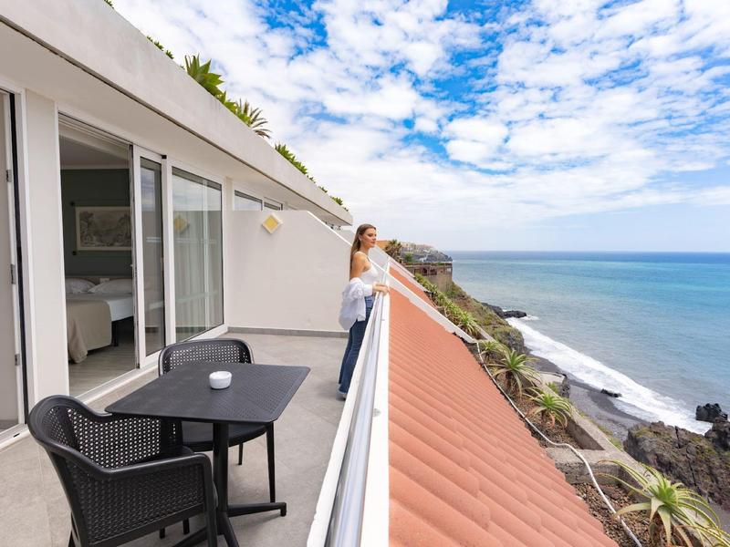 Femme profitant de la vue sur la mer depuis le balcon de l'hôtel avec table et deux chaises.