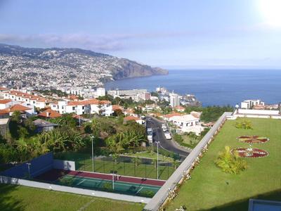 Vista de una ciudad costera con casas, mar y áreas verdes en un día despejado.